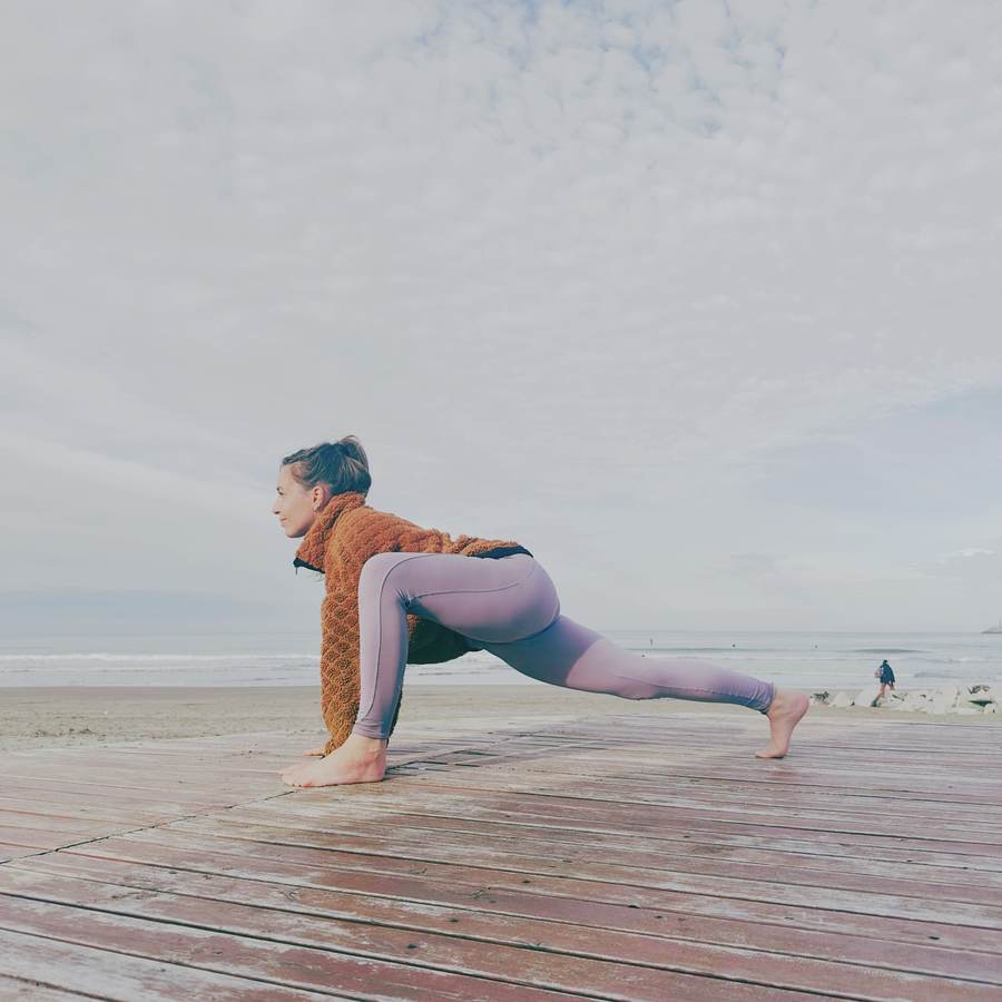 Profesora en una postura de yoga sobre una plataforma de madera, frente al mar
